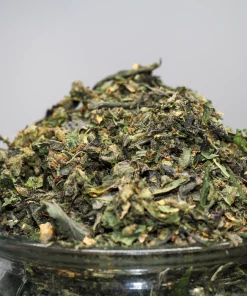 Close-up of a cannabis nugget piled on a glass jar, showing green leaves and frosty trichomes with orange hairs.