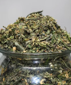 Pile of chopped cannabis leaves and buds on a glass jar, with a Kush Buddy watermark in the corner.