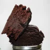 Close-up of dark, crumbly brownie pieces stacked on a metal lid against a light gray background.