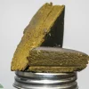 Close-up of a rough, brownish-gold textured chunk resting on a silver metal threaded cap against a pale background.