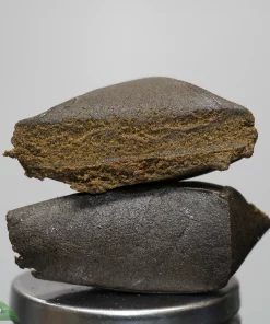 Close-up of a stack of dark brown stones balanced on a small metal pedestal against a gray background.
