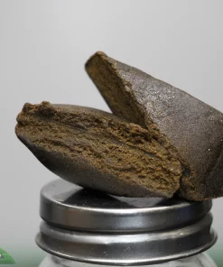Close-up of a dark chocolate brownie stacked on a metal pedestal, with a Kush Buddy watermark in the lower-left corner.