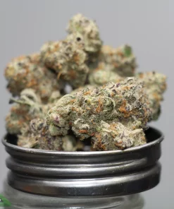 Close-up of frosty cannabis buds stacked in a metal grinder, with Kush Buddy watermark in the corner.