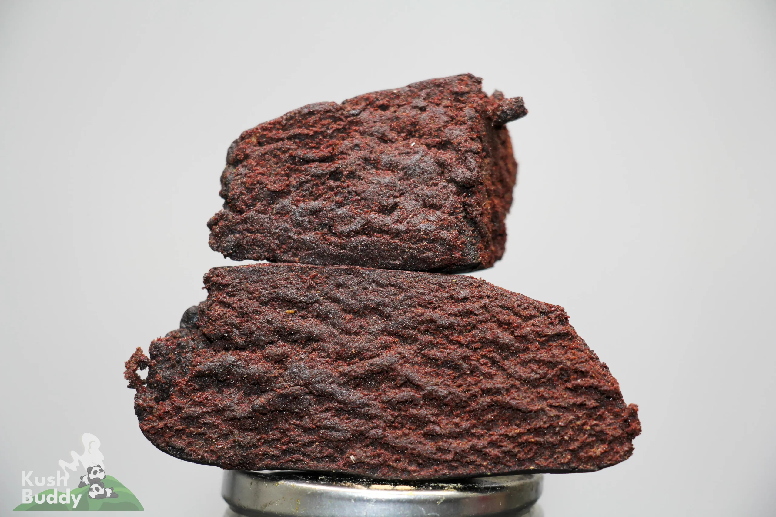 Stack of dark chocolate brownies stacked on a metal bottle cap, with a Kush Buddy watermark in the corner.