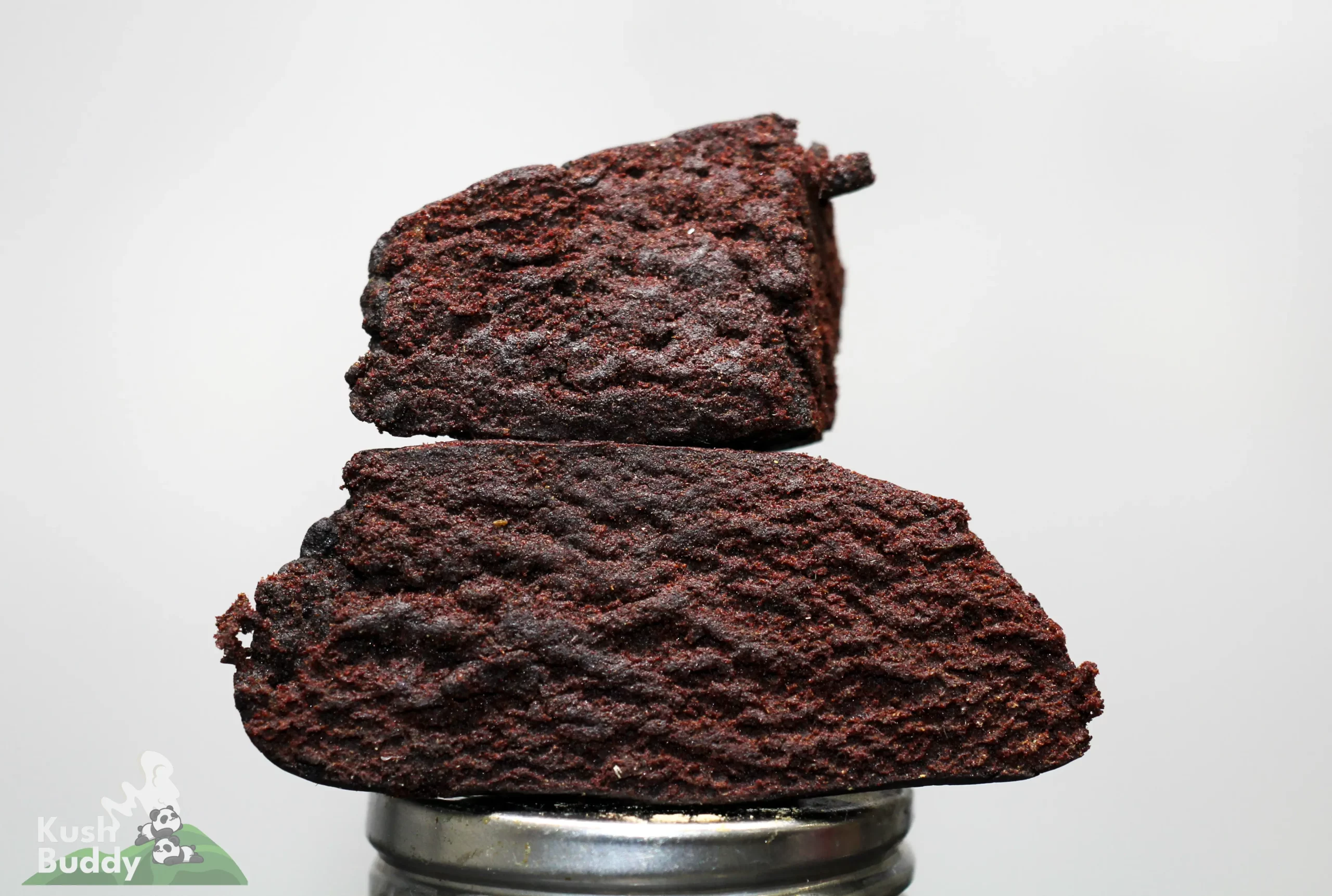 Stack of dark chocolate brownies stacked on a metal pedestal, with a Kush Buddy watermark in the bottom-left corner.