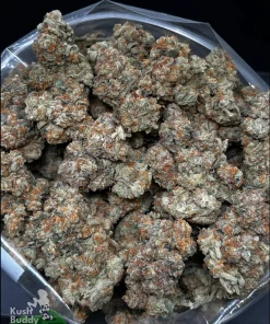 Close-up of dense cannabis buds with orange hairs inside a clear plastic bag; green and frosty with a rock-like texture.