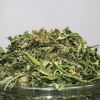 Close-up of dried cannabis buds piled on a glass jar, showing green leaves and orange hairs.