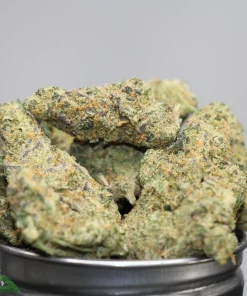 Close-up of frosty green cannabis buds with orange hairs in a metal grinder, showing dense texture and trichomes.