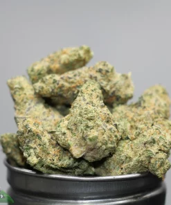Close-up of cannabis buds with frosty crystals in a metal grinder, green with orange hairs, brand watermark visible (Kush Buddy).