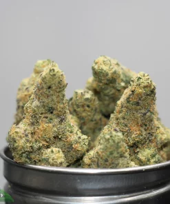 Close-up of frosty cannabis buds in a metal container with a Kush Buddy watermark in the corner.