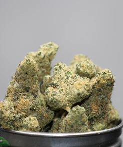 Close-up of frosty cannabis buds spilling from a metal grinder, showing dense trichomes and orange hairs